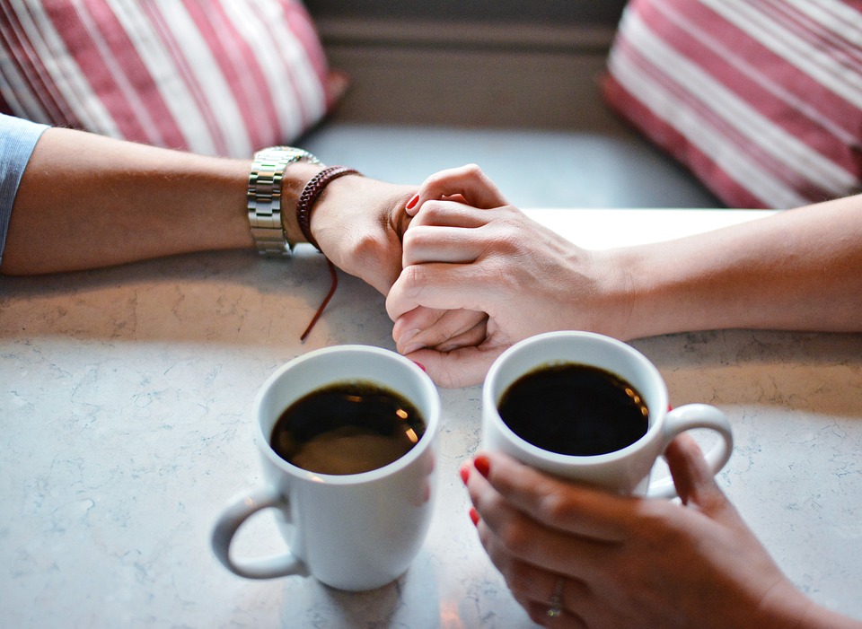 Kaksi kahvikuppia ja kädet, jotka pitävät toisistaan kiinni