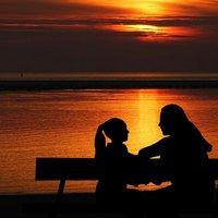 Lapsi ja aikuinen istuvat penkillä auringon laskiessa