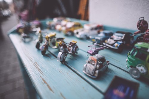 lasten leluja pöydällä rivissä: pikkuautoja ja moottoripyöriä.
